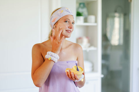 Woman using the Cleansing Balm with Next Stop Glowing Beauty headband, wrap, and wristlets.